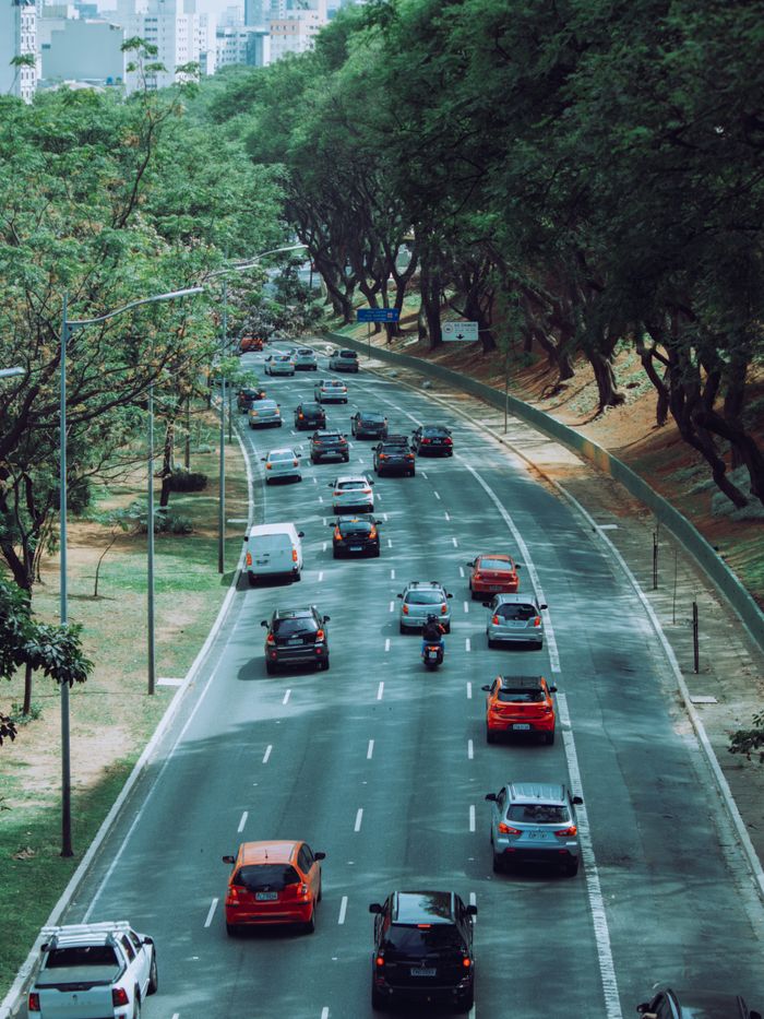 Aerial view of urban traffic on a tree-lined road with vibrant green scenery.