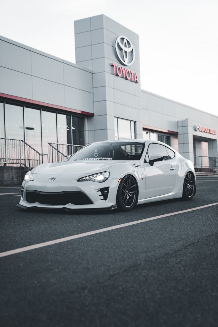 A white sports car prominently displayed outside a modern Toyota dealership building.